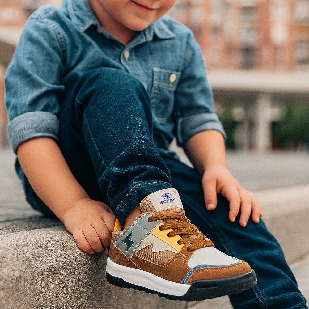 Child wearing a blue denim shirt and brown sneakers with yellow accents, sitting on a concrete surface.