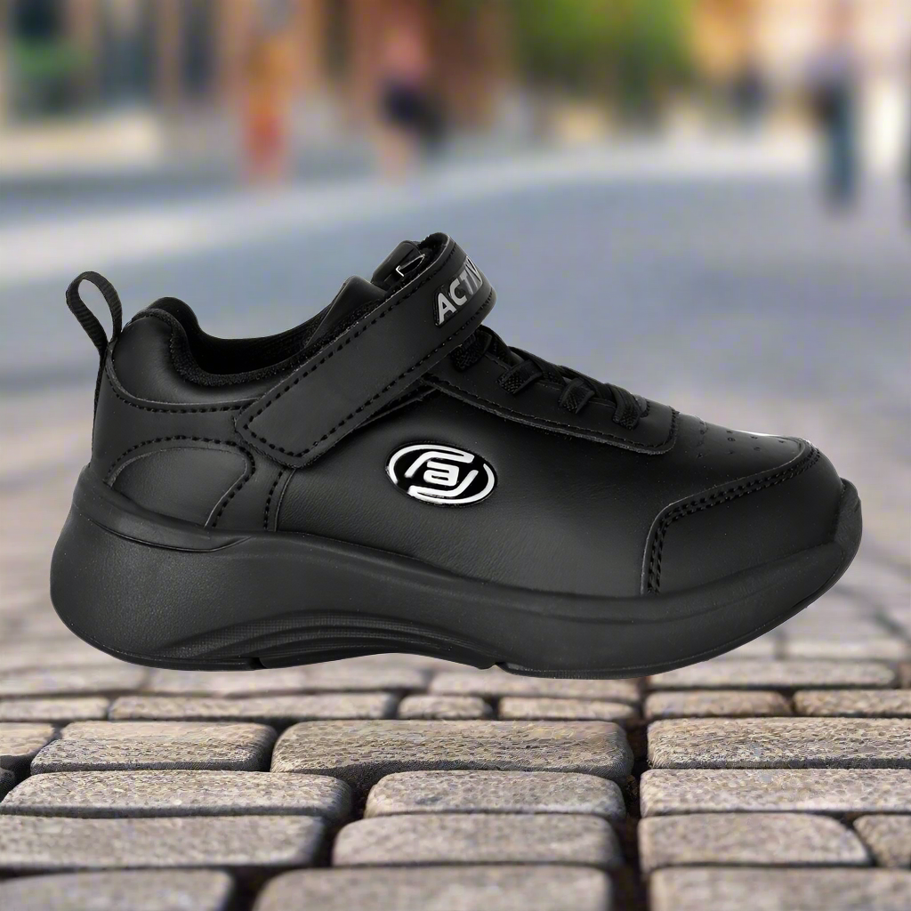 Black children's athletic shoe with a visible brand logo on a blurred street background