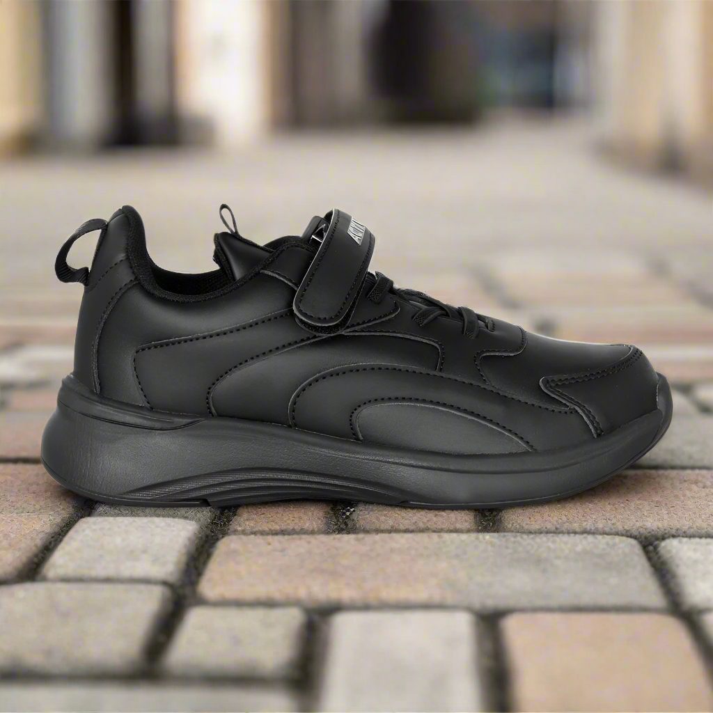 Black sneaker with velcro straps on a stone pavement