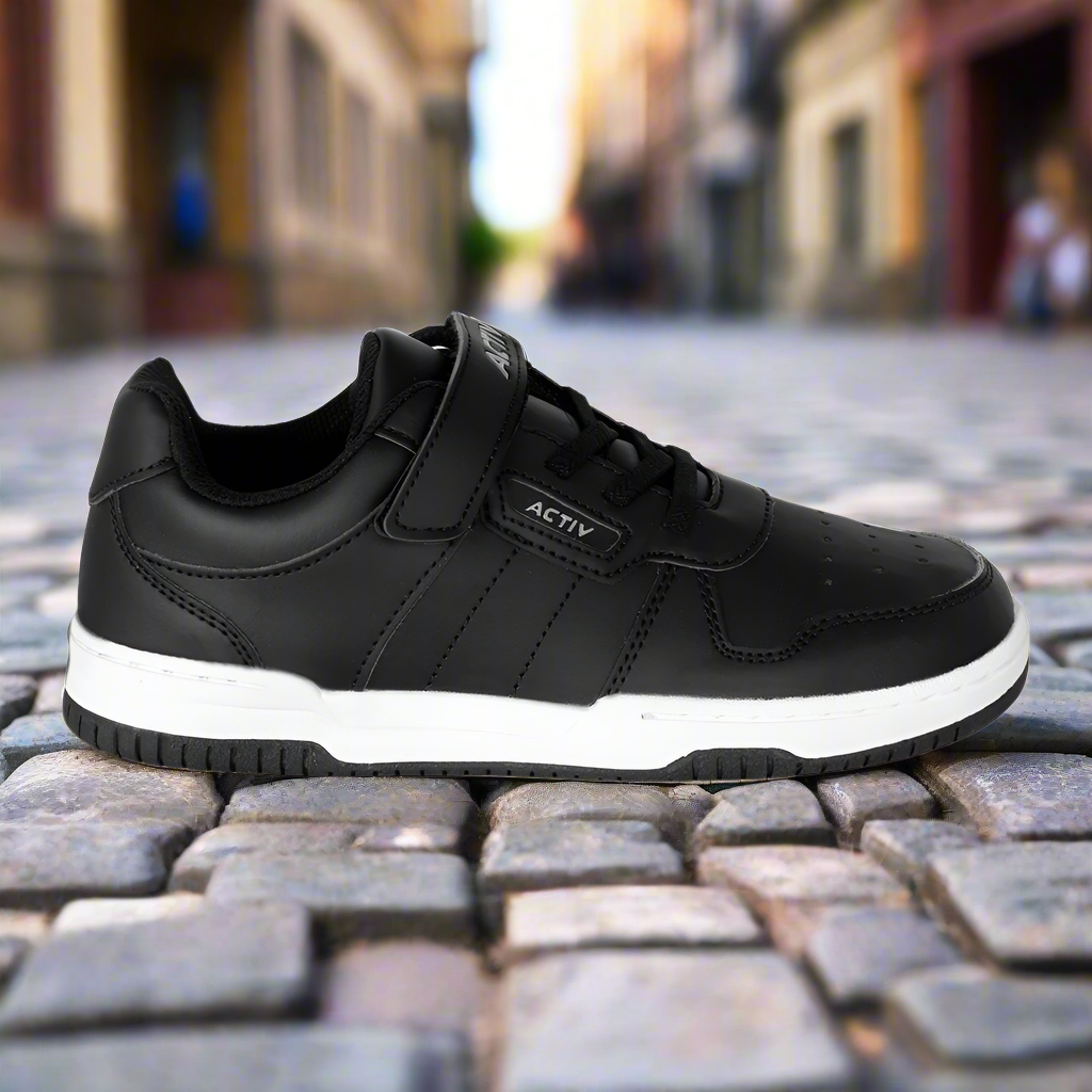 Black sneaker with white sole on a cobblestone street