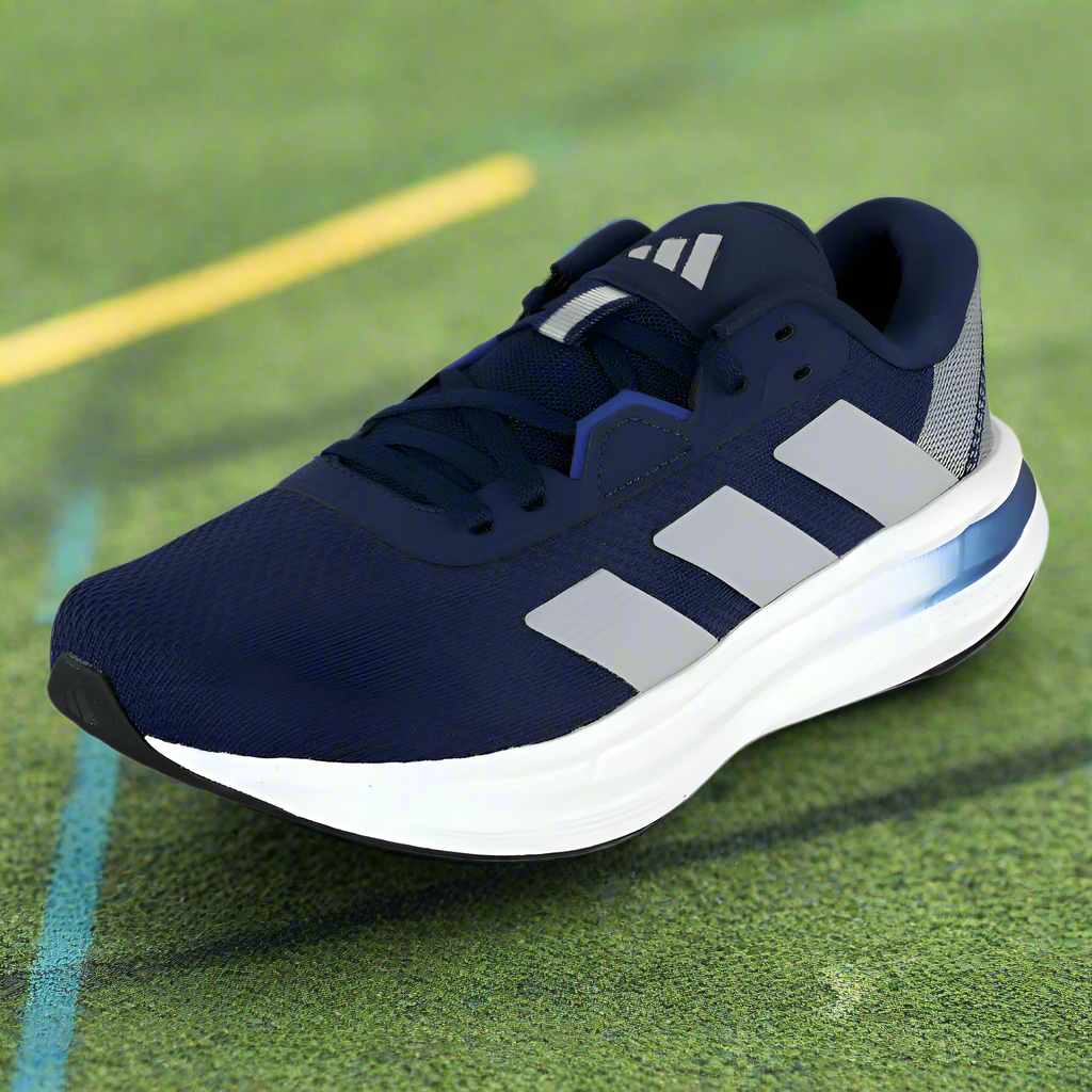 Navy blue running shoe with white stripes on a green sports field background